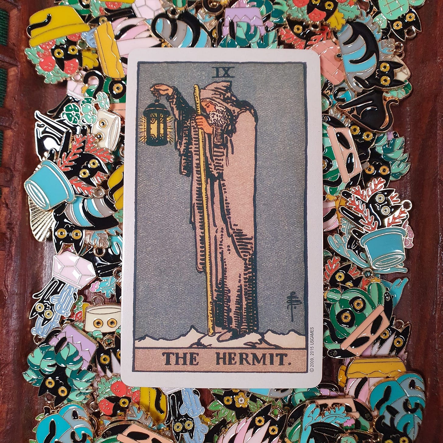 The Hermit tarot card from the Rider-Waite-Smith deck, photographed by Finbarre Snarey for Tarot DMs, resting on a colourful pile of black cat enamel pins. The Hermit tarot card from the Rider-Waite-Smith deck, photographed by Finbarre Snarey for Tarot DMs, resting on a colourful pile of black cat enamel pins.