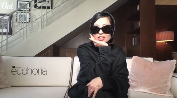 This may contain: a woman sitting on top of a white couch wearing sunglasses and a black hoodie