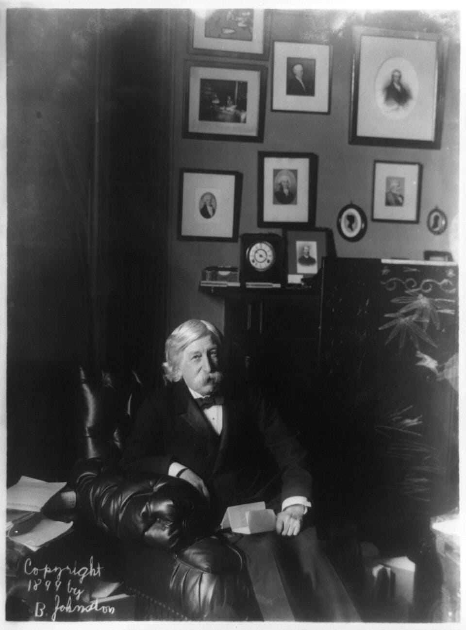 Black and white photograph. An old man with white hair and a thick mustache, Melville Fuller, sits in an overstuffed leather chair. Black and white photograph. An old man with white hair and a thick mustache, Melville Fuller, sits in an overstuffed leather chair.