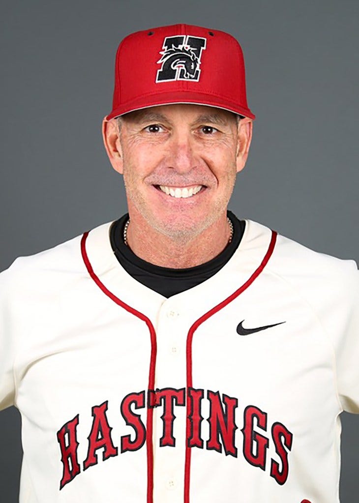 Victor Rojas, entraîneur-chef de l'équipe de baseball des Hastings Broncos, sourit en portant une casquette de baseball rouge avec un logo de bronco noir et blanc et un maillot de baseball blanc avec l'inscription « HASTINGS » en lettres rouges. Victor Rojas, entraîneur-chef de l'équipe de baseball des Hastings Broncos, sourit en portant une casquette de baseball rouge avec un logo de bronco noir et blanc et un maillot de baseball blanc avec l'inscription « HASTINGS » en lettres rouges.