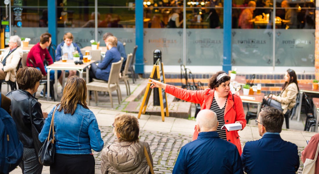 A woman in a red coat pointing to the left, with a crowd of people in front of her