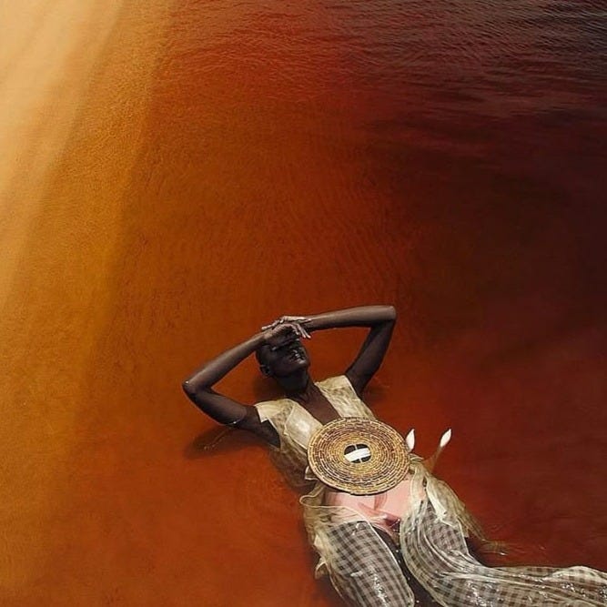A woman resting peacefully while floating in reddish-amber water next to a sandy shoreline, a visual metaphor for rest, surrender, and mental health peace.