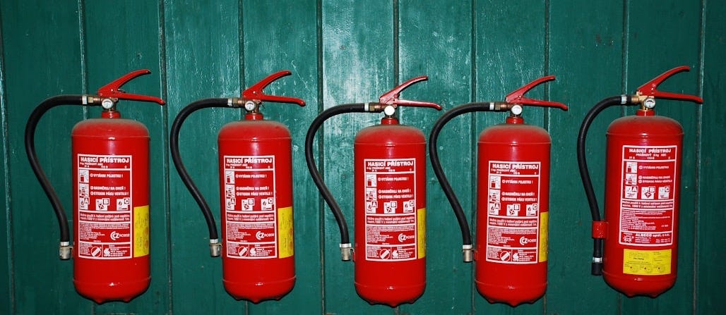 four fire extinguishers lined up against a green wall four fire extinguishers lined up against a green wall