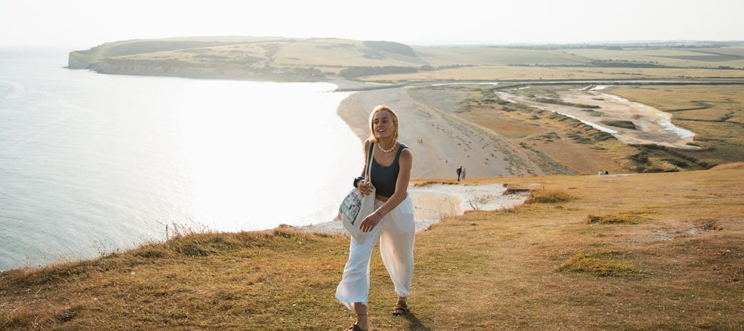 A woman standing on top of a hill next to the ocean