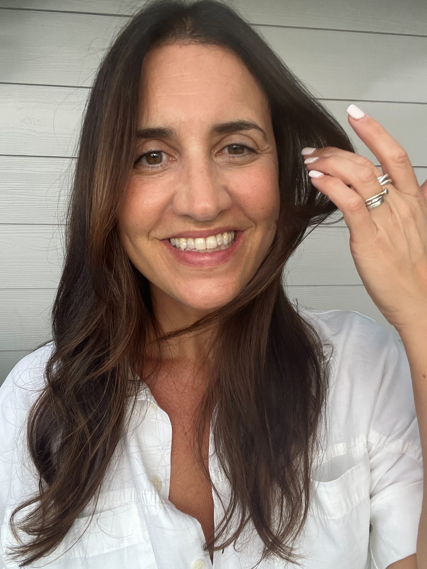 A smiling professional beauty editor with long brown hair wearing a white button-down shirt against a neutral background.