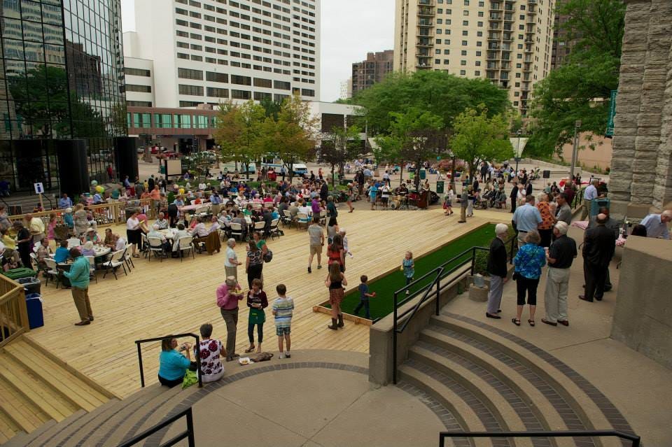 People gather at tables on a large wooden deck outside of a cathedral.