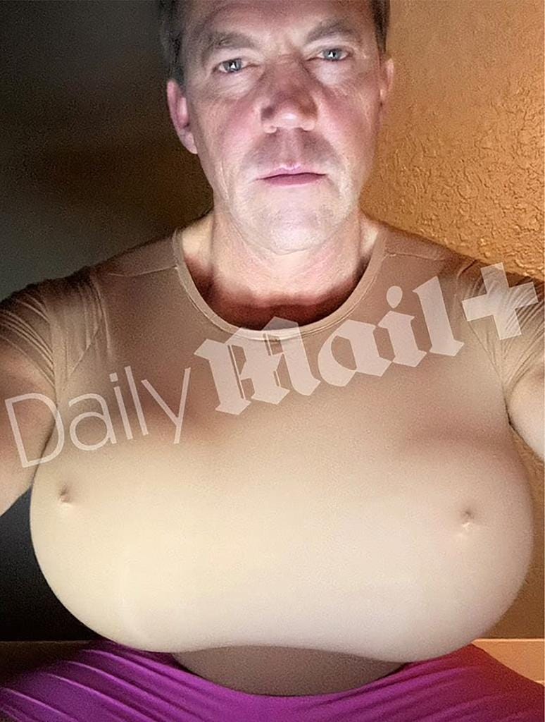 A man wearing a tan shirt over large prosthetic breasts, with the "Daily Mail+" watermark across his chest.