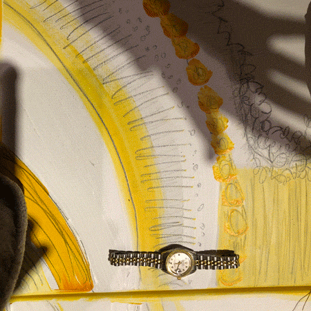 Rainbow Squared, Year 5, Piece Fourteen: 21. Yellow Black White by Janet Self. A photo animation of a shadow of hand continually grasping at a silver wrist-watch on a painted white background with pencil sketches and yellow paint lines on top of it.