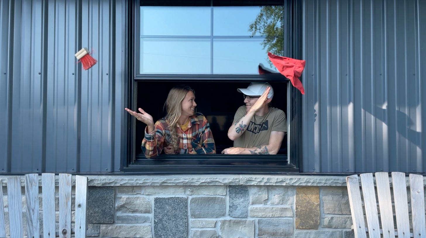 a couple standing in an open window looking at each other, throwing a small brush and rag out the window