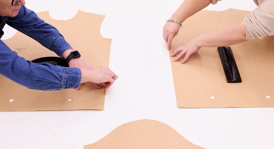 Three people cutting out brown paper t-shirt templates on white fabric