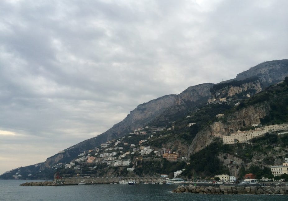 A view of the Amalfi coastline from Positano with homes in the distance all along the cliffside and the ocean in the foreground. A view of the Amalfi coastline from Positano with homes in the distance all along the cliffside and the ocean in the foreground.