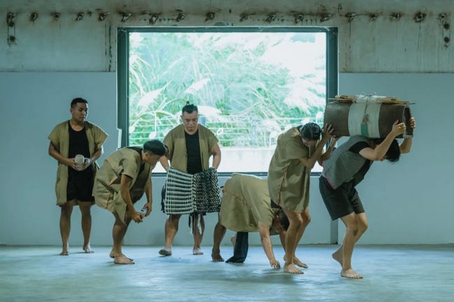 Les danseurs de TAI sur scène, représentant une scène de vie, l'un d'entre eux portant du matériel comme un sherpa Les danseurs de TAI sur scène, représentant une scène de vie, l'un d'entre eux portant du matériel comme un sherpa
