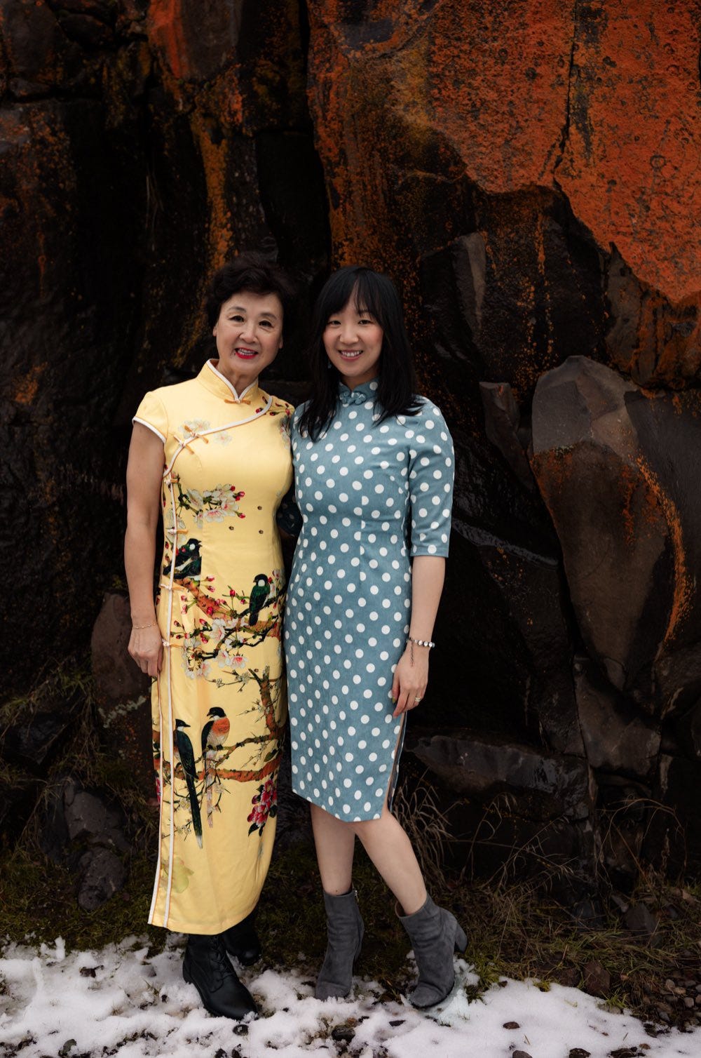 My beautiful mother standing next to me in front of a red rock on the snow.