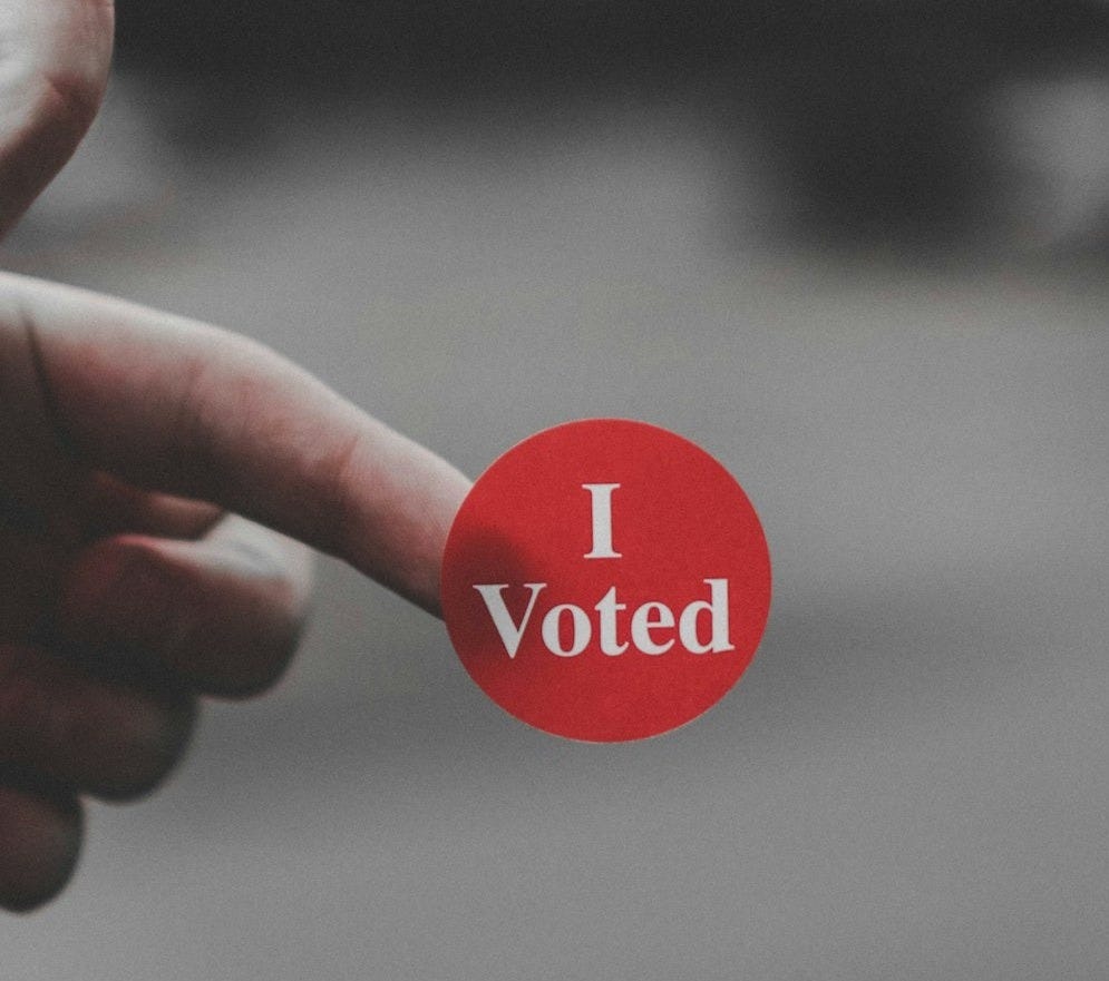 a hand holding a red button that says i vote a hand holding a red button that says i vote