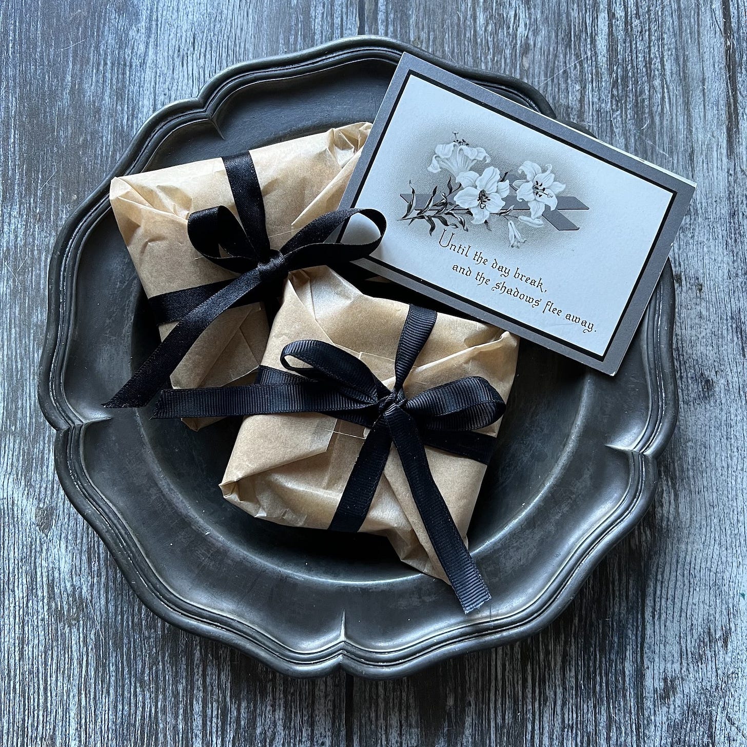 2 brown paper packages tied with black ribbon on a silver pewter plate with a funeral card