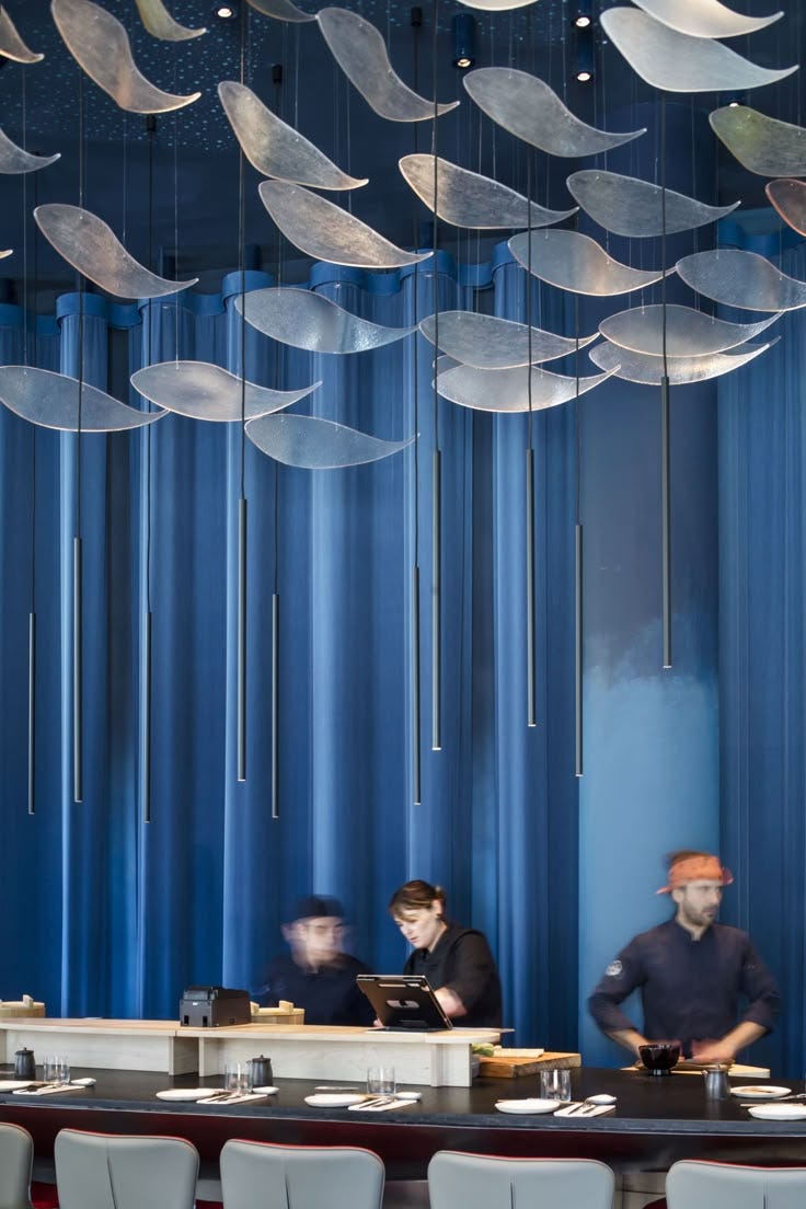 This may contain: three people sitting at a table in front of blue curtained walls with suspended lights