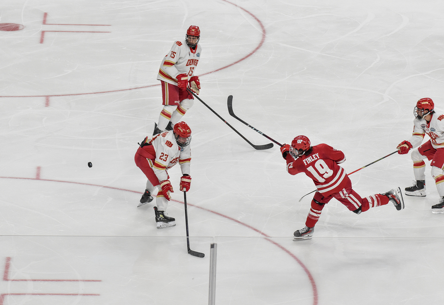Wisconsin forward fires puck while being defended by three Denver Pioneer players at NCAA Mens Frozen Four.