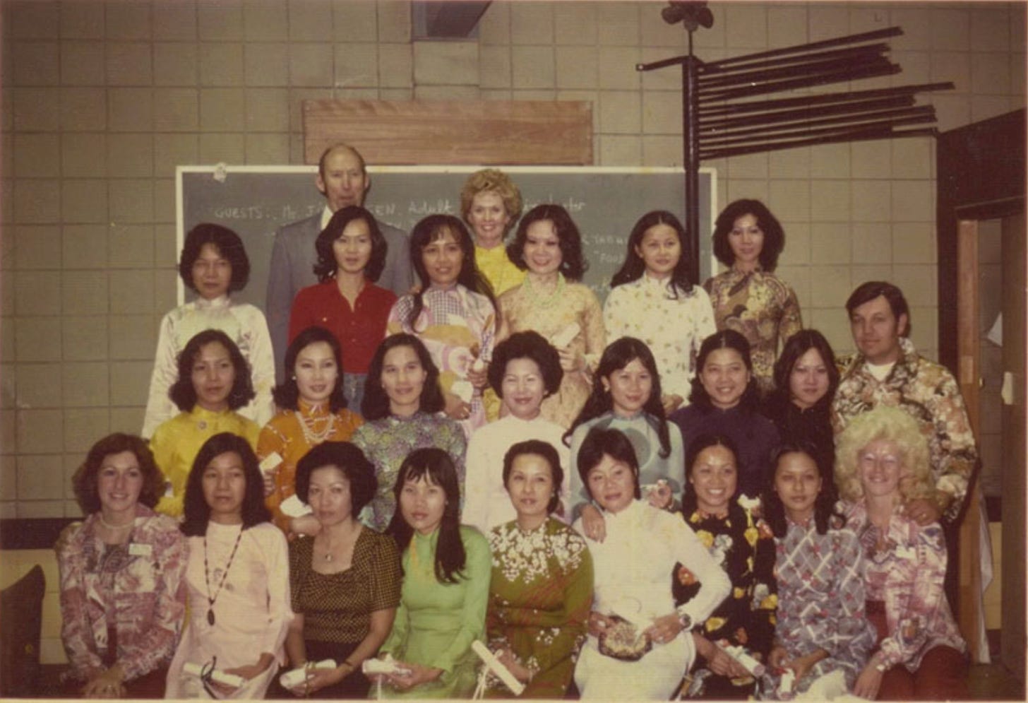 Color photograph showing a large group of Vietnamese women arranged in three rows, with actress Tippi Hedren standing in the back row. The photo appears to be from the 1970s based on clothing and hair styles. The women wear a variety of patterned dresses and blouses in yellows, reds, and earth tones.