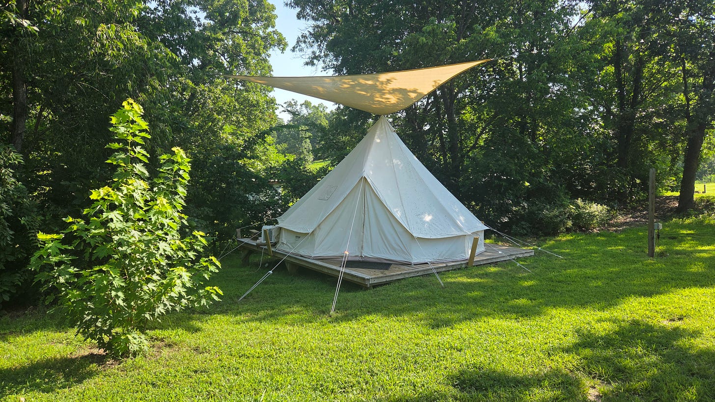 A large tent on a lawn, tucked into some trees