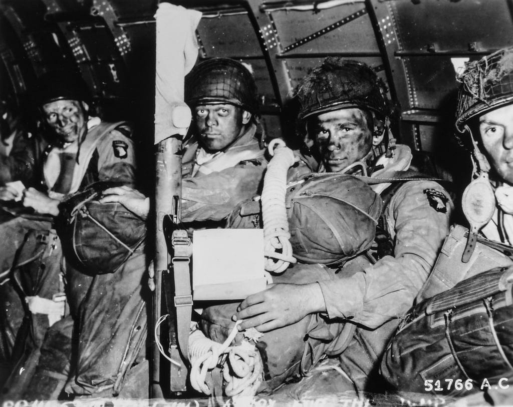 Black and white photo of U.S. Airborne troops on their transport aircraft in full combat gear and parachutes. Their faces reflect the seriousness of the coming operation. The center soldier is holding a copy of General Eisenhower's message to the forces about what is at stake for Operation OVERLORD. Black and white photo of U.S. Airborne troops on their transport aircraft in full combat gear and parachutes. Their faces reflect the seriousness of the coming operation. The center soldier is holding a copy of General Eisenhower's message to the forces about what is at stake for Operation OVERLORD.