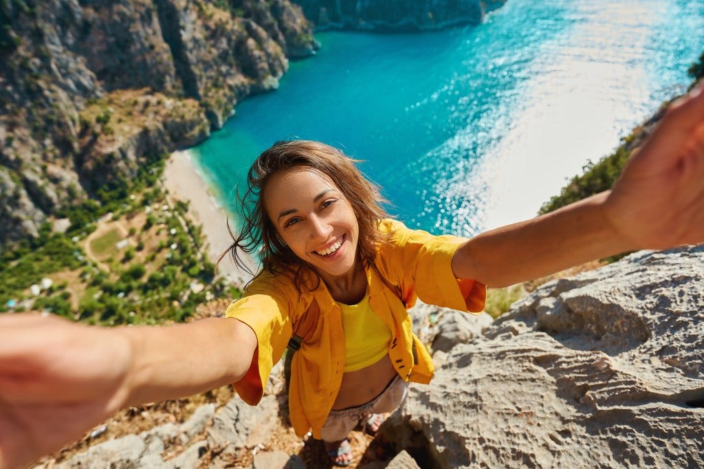 A smiling woman taking a selfie from a cliff overlooking a turquoise bay and beach in Turkey. A smiling woman taking a selfie from a cliff overlooking a turquoise bay and beach in Turkey.