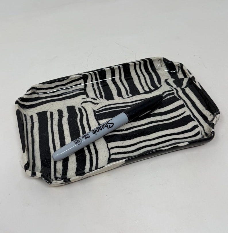 May include: A black and white striped ceramic tray with a black Sharpie pen on top. The pen is labeled 'Sharpie' and 'Fine Point' and has a gray cap.