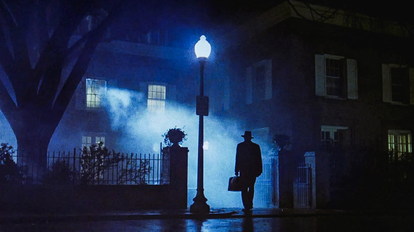 A silhouetted priest stands beneath a glowing streetlamp, facing a fog-drenched Georgetown townhouse with light streaming from an upstairs window. A silhouetted priest stands beneath a glowing streetlamp, facing a fog-drenched Georgetown townhouse with light streaming from an upstairs window.