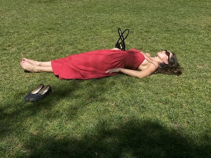 This may contain: a woman in a red dress laying on the grass next to a pair of shoes