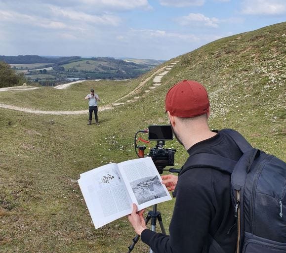 Camera man sets up camera on tripod to record presenter talking to camera on location at Cissbury Ring, Sussex