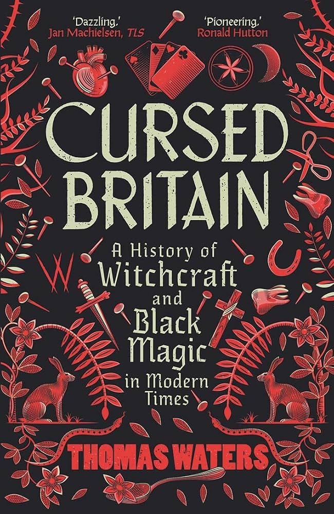 Book cover of Cursed Britain: A History of Witchcraft and Black Magic in Modern Times by Dr Thomas Waters. Cream-coloured gothic lettering stands against a black background, surrounded by intricate red illustrations of magical and folkloric symbols, including a human heart, playing cards, pins, a horseshoe, crescent moon, hares, snakes and flowering plants. Book cover of Cursed Britain: A History of Witchcraft and Black Magic in Modern Times by Dr Thomas Waters. Cream-coloured gothic lettering stands against a black background, surrounded by intricate red illustrations of magical and folkloric symbols, including a human heart, playing cards, pins, a horseshoe, crescent moon, hares, snakes and flowering plants.