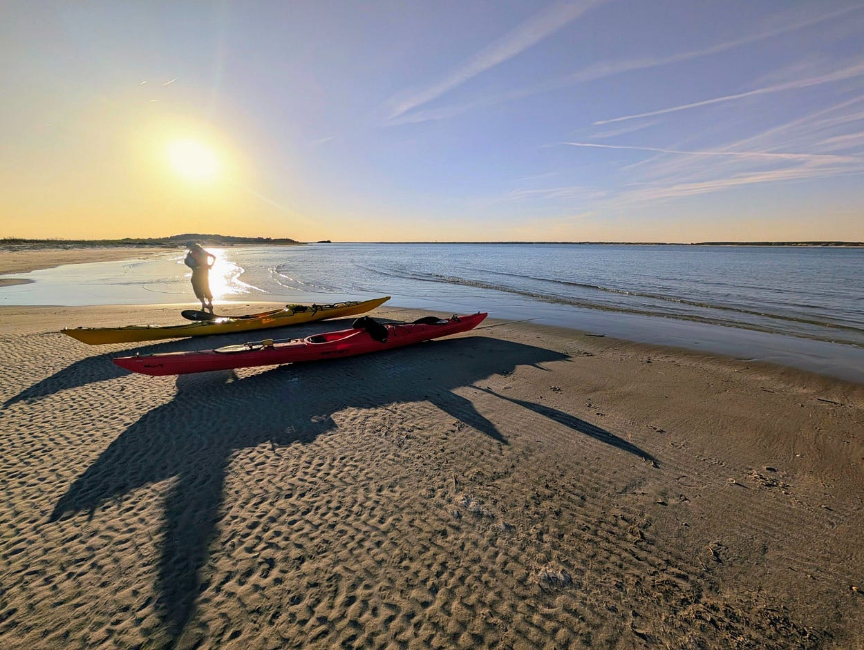 The silhouette of a kayaker and two sea kayaks on a beach in the afternoon sunlight. The silhouette of a kayaker and two sea kayaks on a beach in the afternoon sunlight.