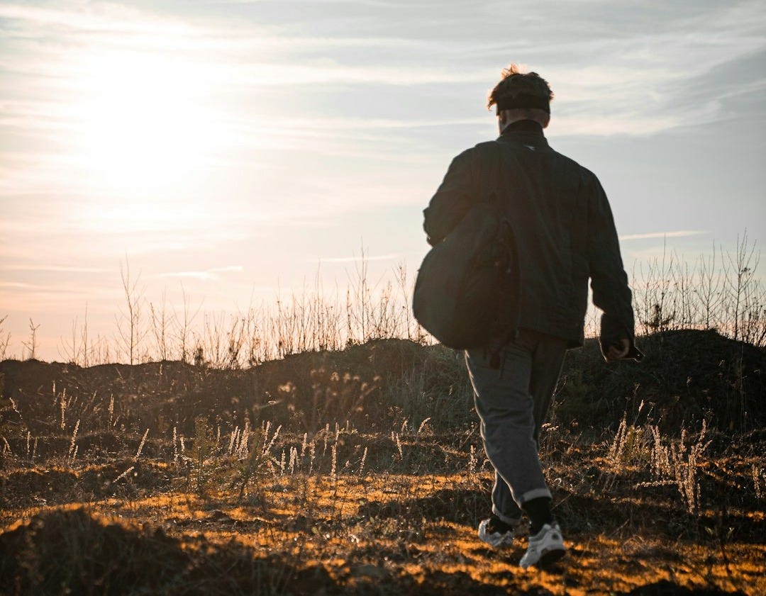 man in black jacket walking on brown grass field during daytime man in black jacket walking on brown grass field during daytime
