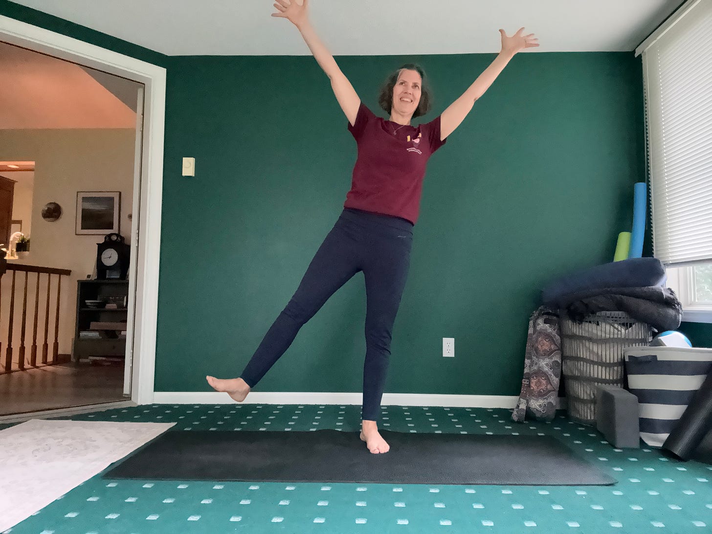 A woman stands on one foot with the other leg raised and arms stretching to the corners of the room