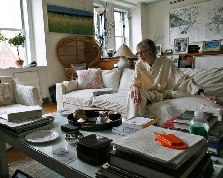 This may contain: an older woman sitting on a couch in front of a table with books and magazines
