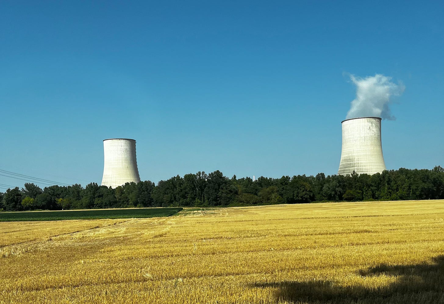Two towers with one emitting steam/smoke in the countryside