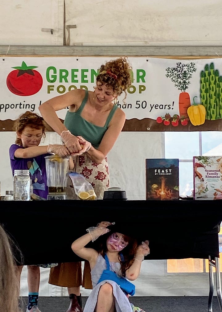 Chef Emma Frisch on stage demonstrating how to make a recipe for Golden Tahini Dressing with her daughters.