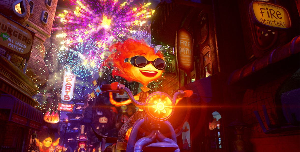 In a scene from the Pixar Animation Studios feature Elemental, Ember, a  female fire person, rides a motorcycle through Element City at night, with  fireworks going off in the sky behind her.