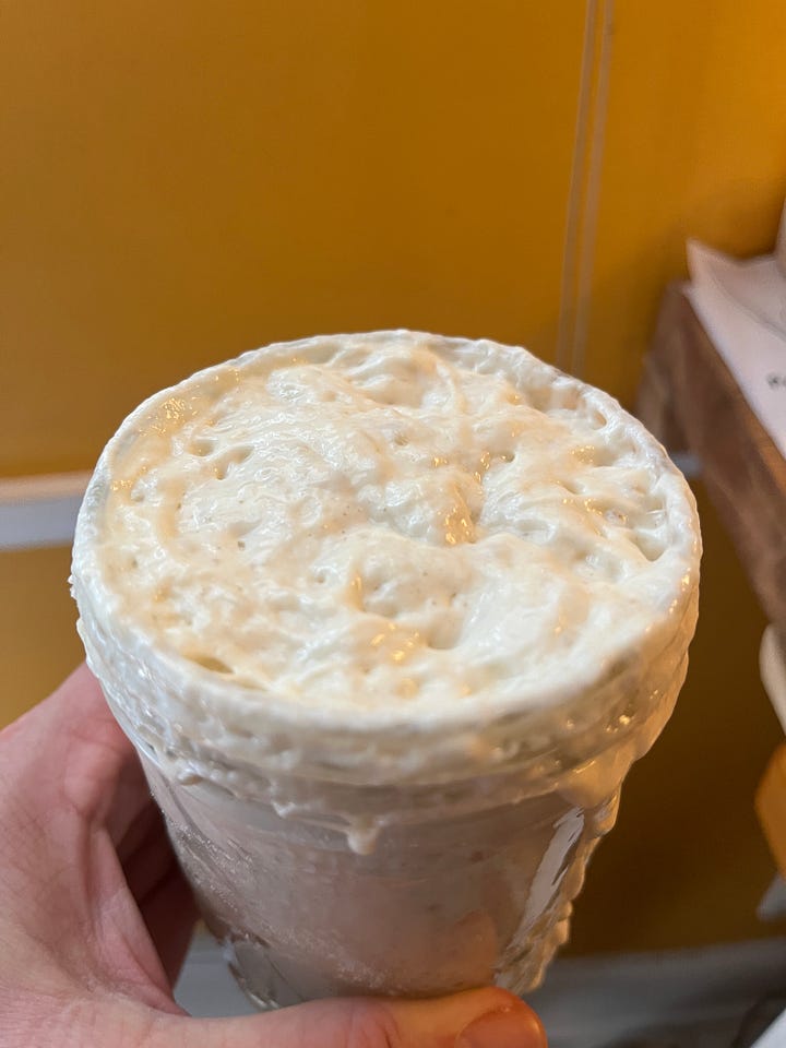 On the left, a jar on top of my fridge that has overflowed with starter, which looks like a thick pancake batter. On the right, I'm holding the open jar, which is filled to the brim with starter, which is bubbling and frothing