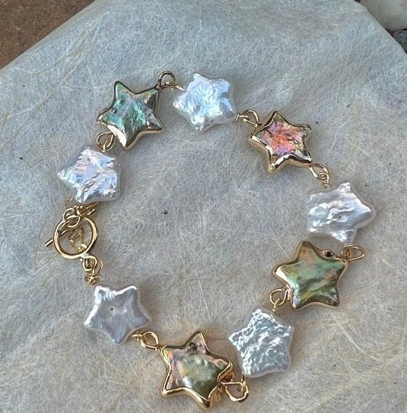 May include: A gold chain bracelet with white and iridescent star-shaped pearl charms