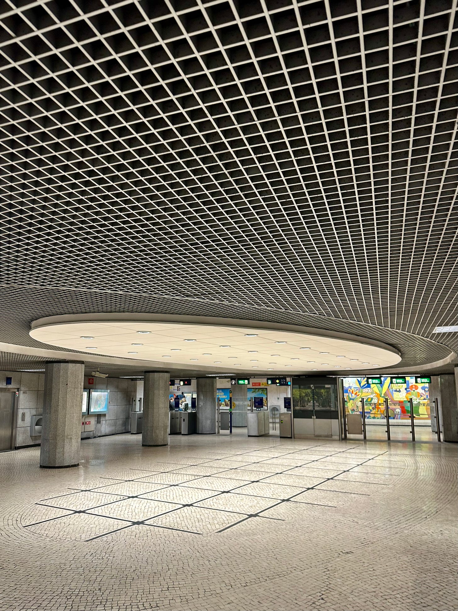 An accidental capture I got in a Lisbon metro station ticket hall where the circular light feature seems to mirror the oval arrangement of titles on the floor.