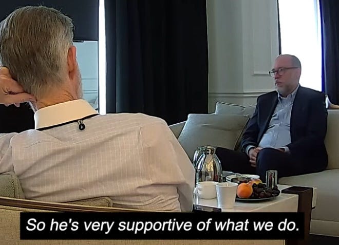 Video screenshot of Russell Vought, wearing a blue suit and light blue dress shirt with no tie, sitting on a couch talking to reporters pretending to be donors. Dialogue caption reads 'So he's very supportive of what we do.' Video screenshot of Russell Vought, wearing a blue suit and light blue dress shirt with no tie, sitting on a couch talking to reporters pretending to be donors. Dialogue caption reads 'So he's very supportive of what we do.'