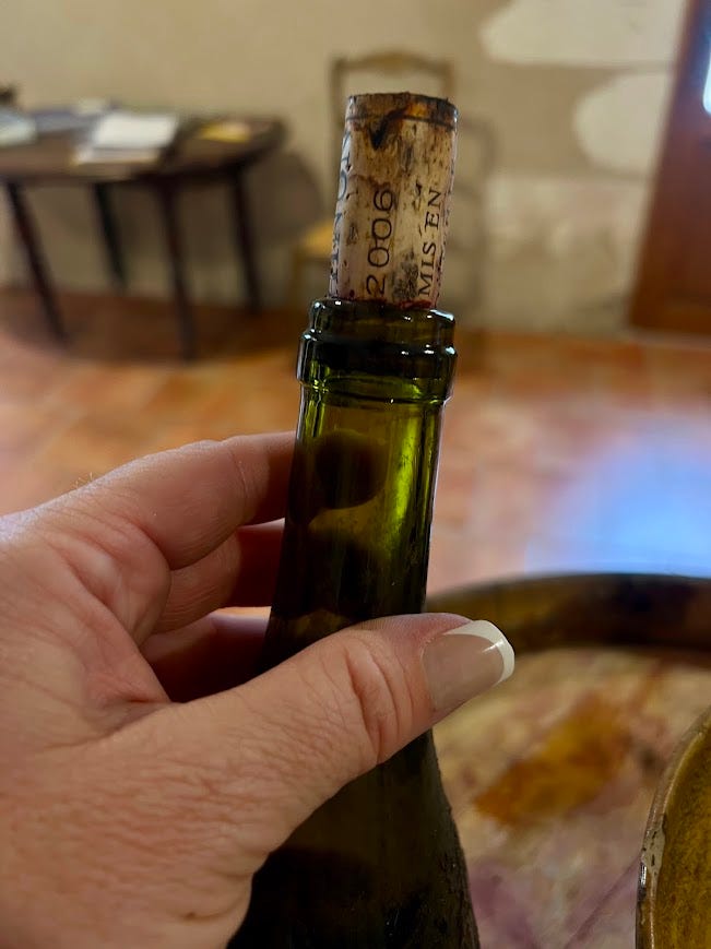 A hand holding an old, partially aged wine bottle marked '2006,' with a weathered cork stamped 'mis en' still in the neck.