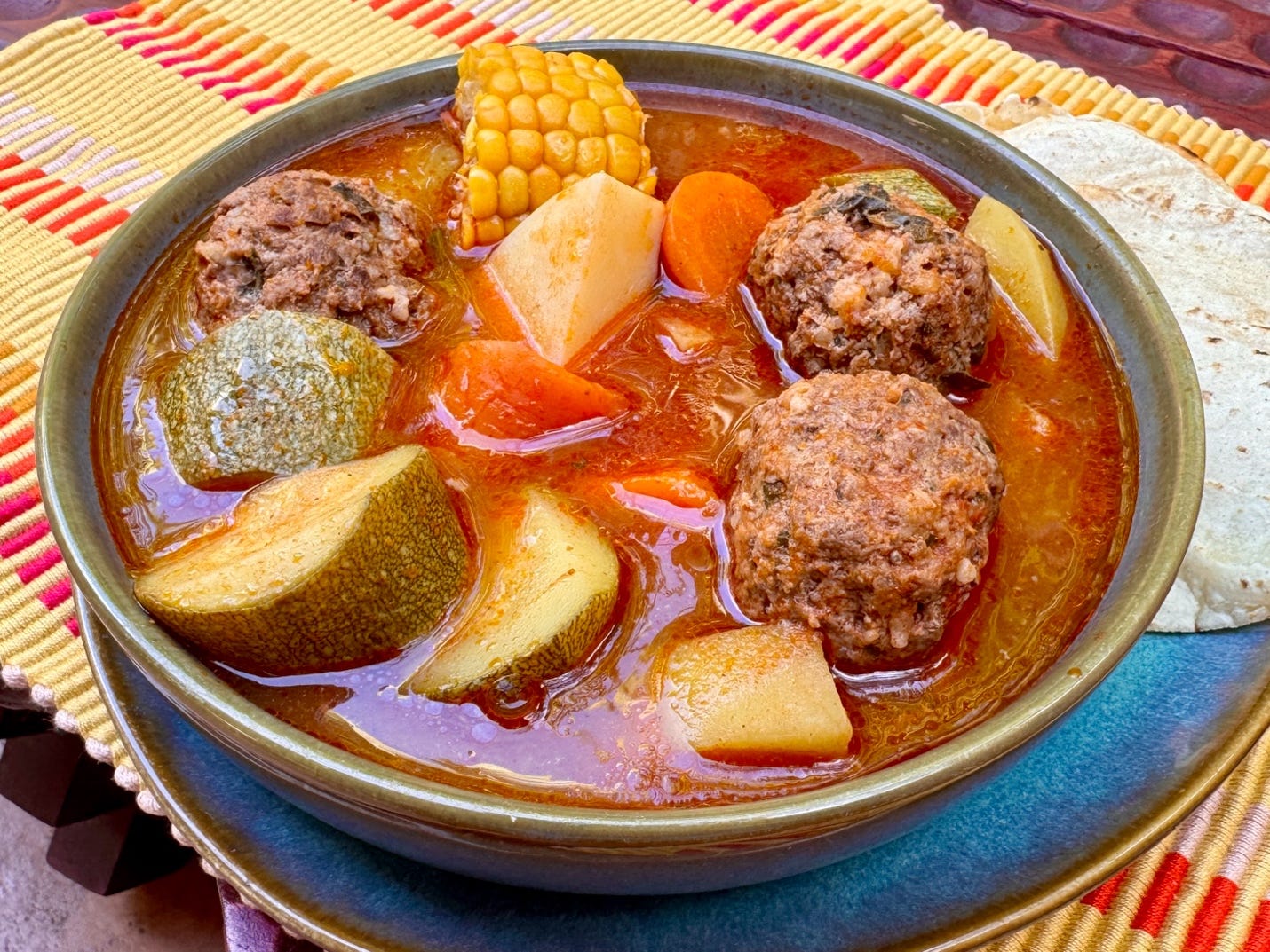 Close-up of caldo de albóndigas with meatballs, zucchini and carrots in tomato broth.