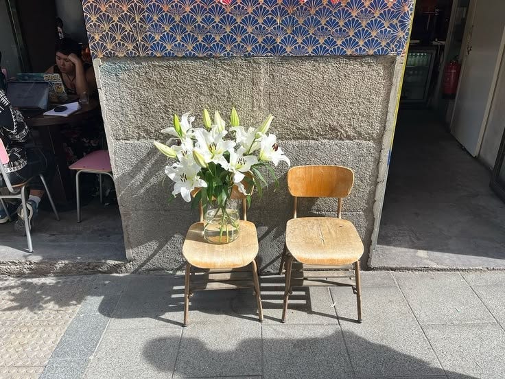 This may contain: two wooden chairs sitting next to each other with flowers in the vase on top of them