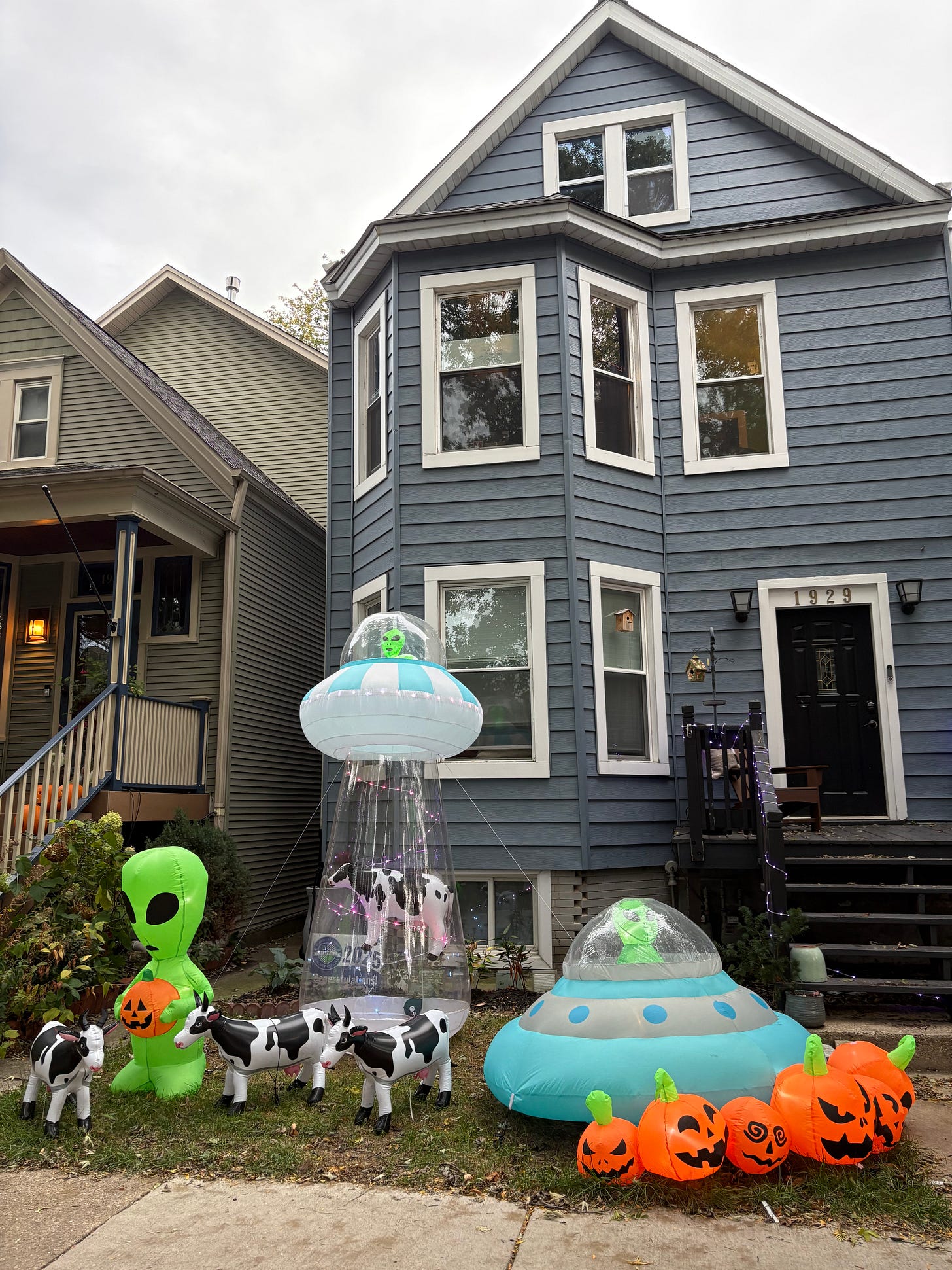 Grey house surrounded by inflatable aliens, cows, and pumpkins