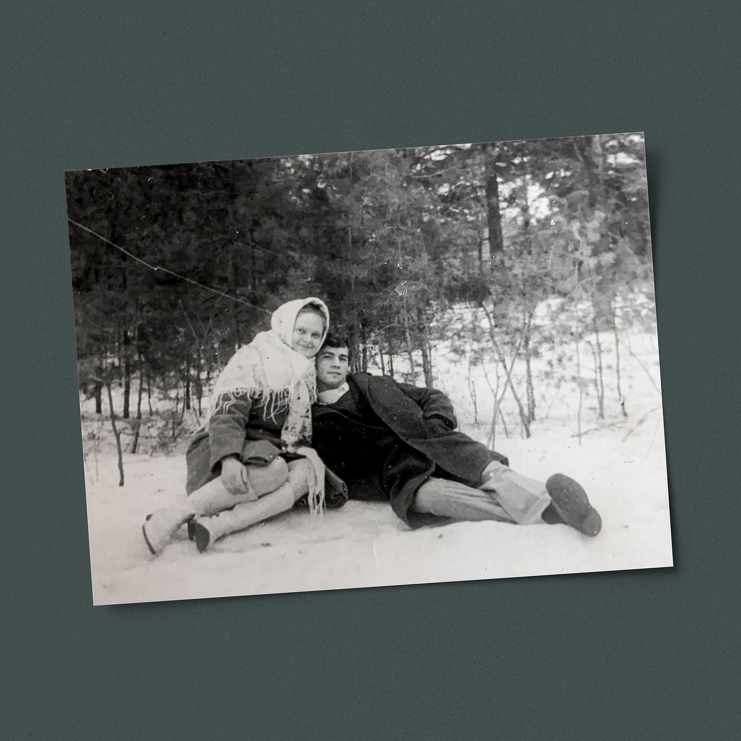 Photo of couple sitting on the snow outside with green background.