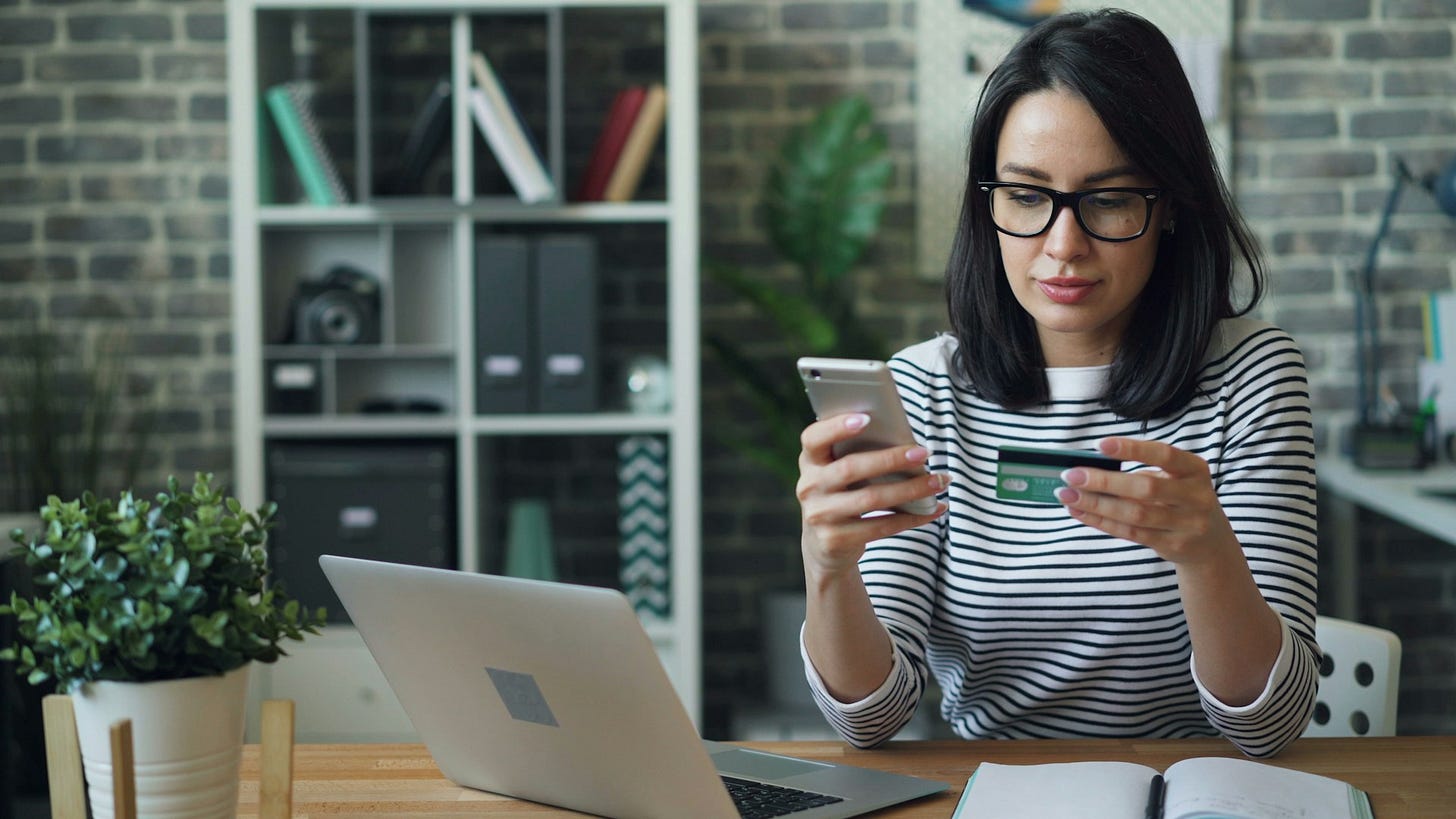 Woman shops online using a smartphone and credit card while sitting at a desk with a laptop, illustrating the convenience and choices of modern ecommerce. Photo by Vitaly Gariev on Unsplash