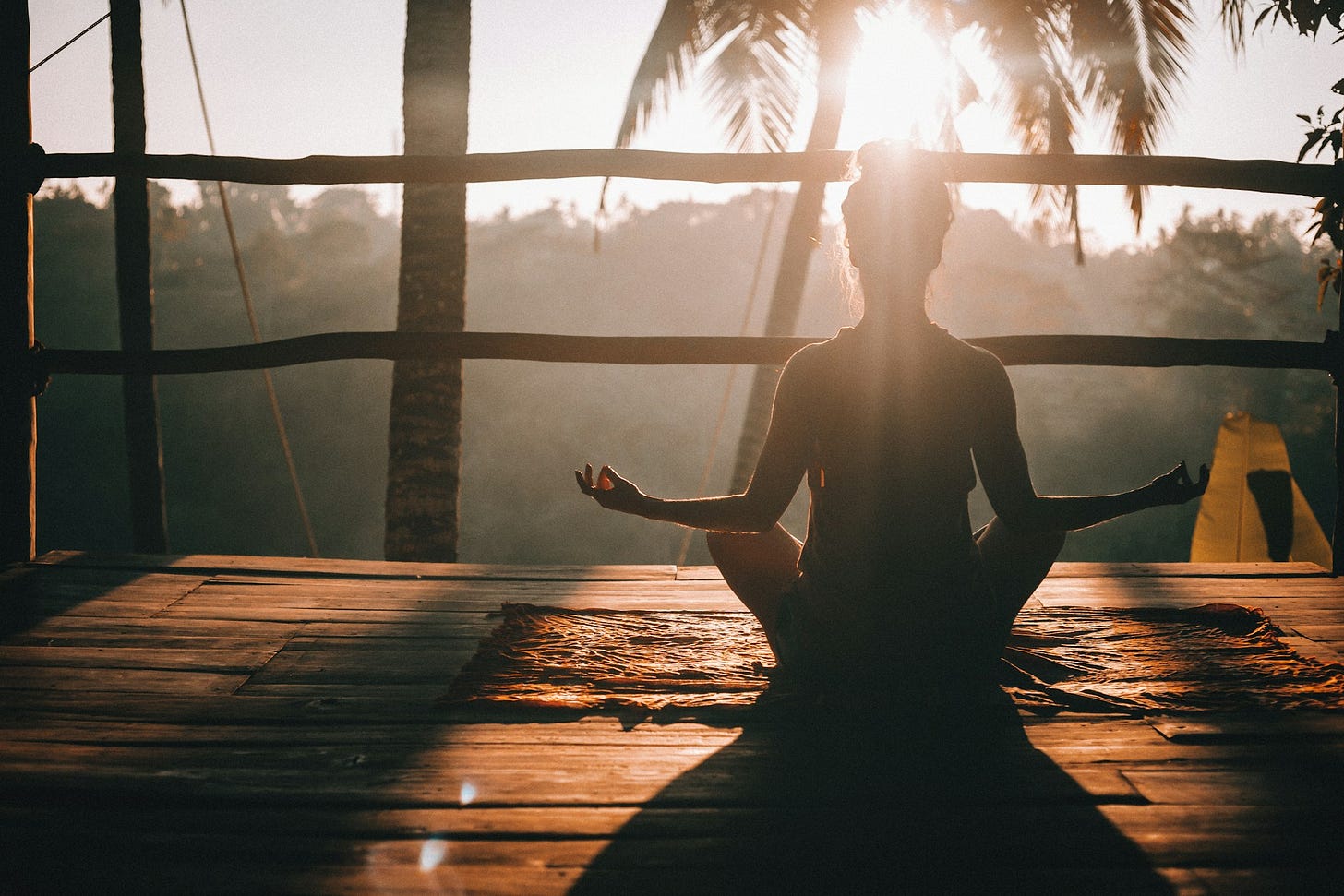 A person practices meditation at sunrise on a wooden deck, symbolizing balance, mindfulness, and self-care. Photo by Jared Rice on Unsplash