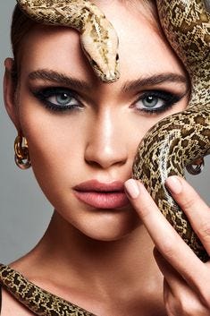 This may contain: a woman holding a snake over her face and looking at the camera with an evil look on her face