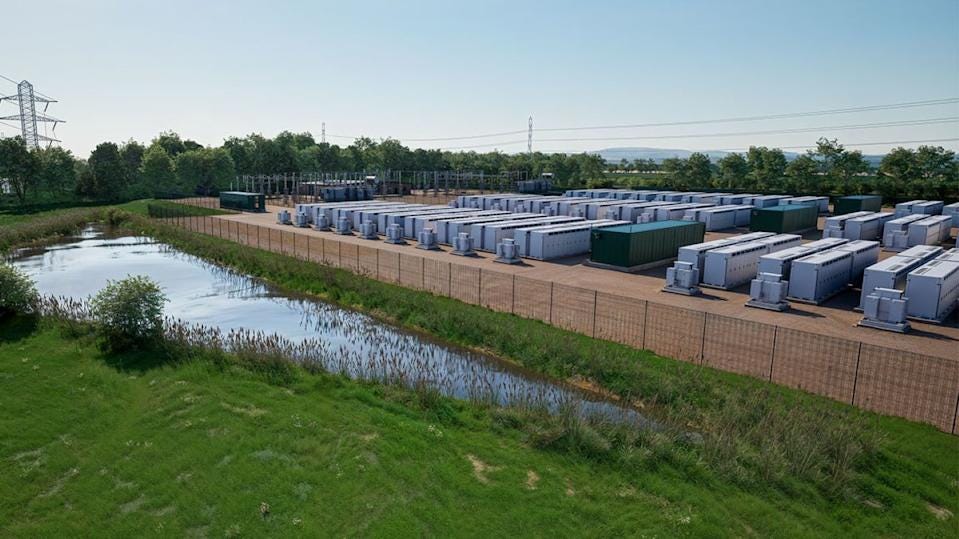 Large grid-scale battery storage facility with rows of container units near power lines.